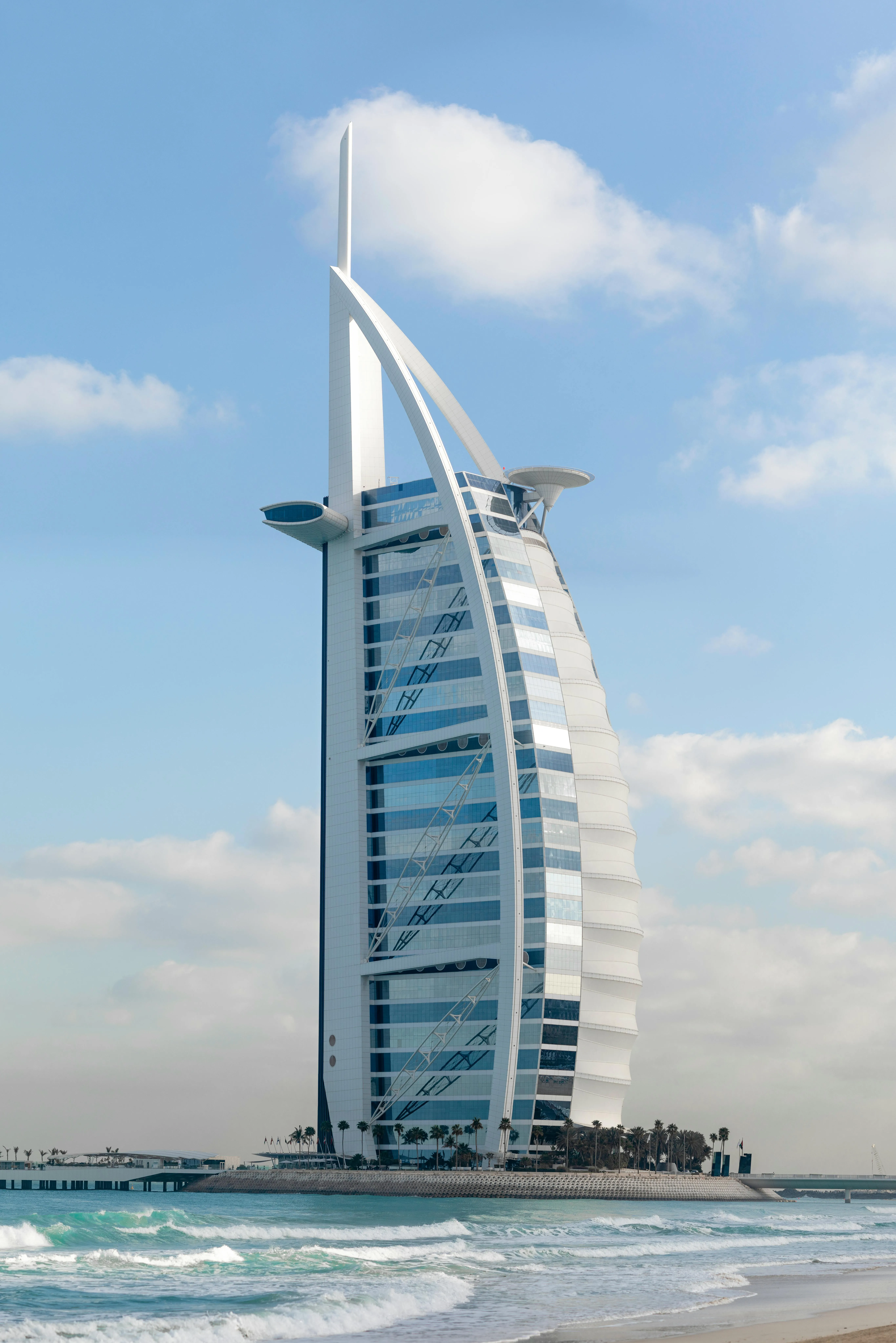 Burj Al Arab — charakterystyczny hotel w kształcie żagla na wybrzeżu Dubaju, widok z plaży z falami na pierwszym planie.